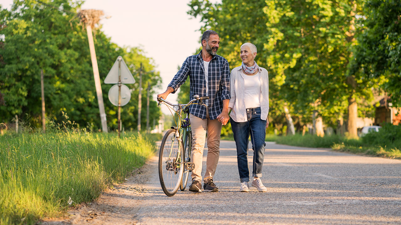 Elderly couple walking on the road while the man holding the bike